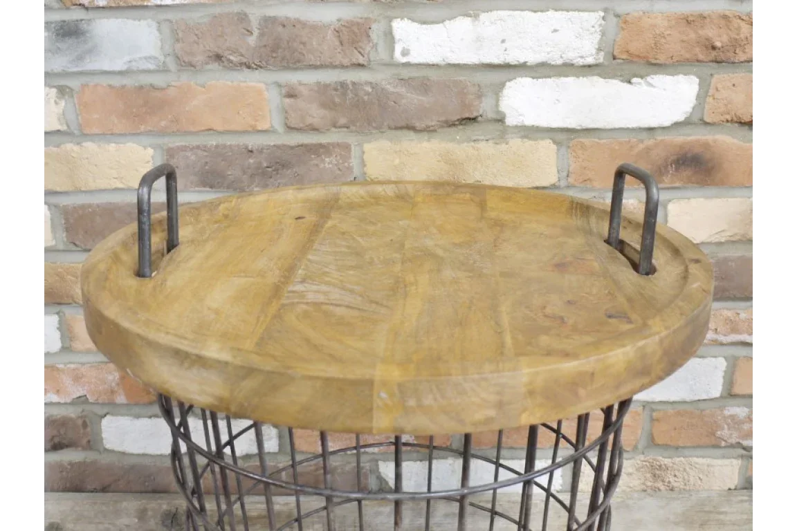 Round wire basket side table with wooden top and metal handles against brick wall