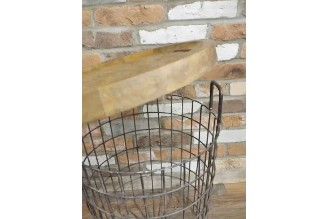Round wire storage basket with wooden lid, lid partially open, placed against brick wall