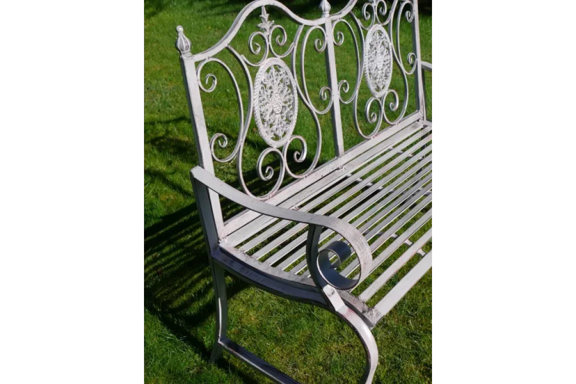 White metal garden bench with ornate backrest on grass