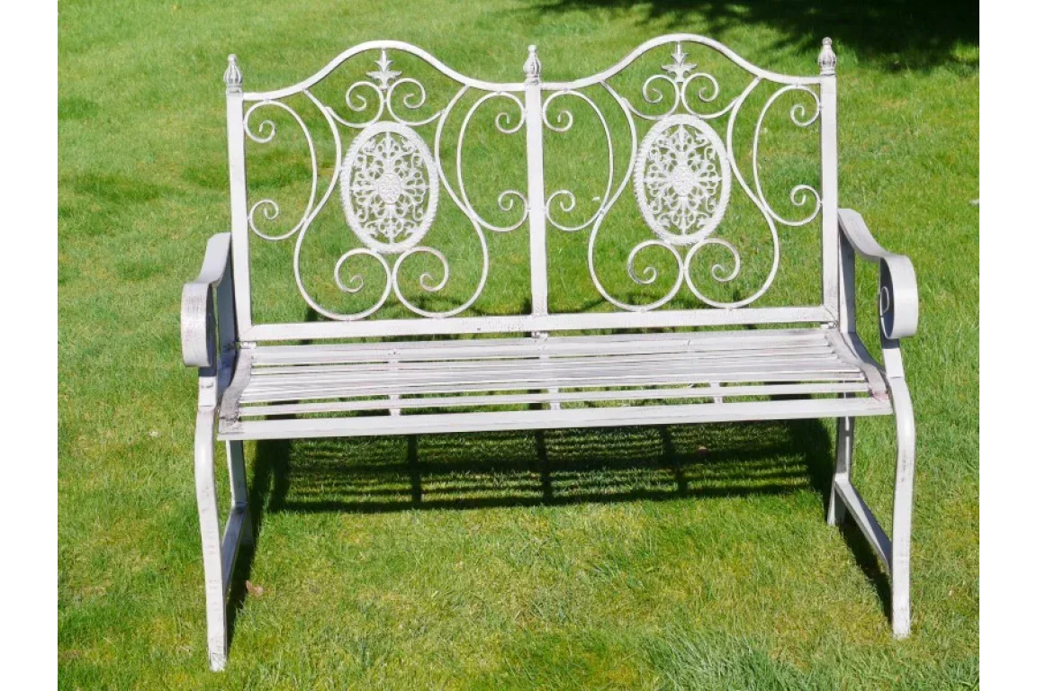 White metal garden bench with ornate scrollwork design on grass lawn