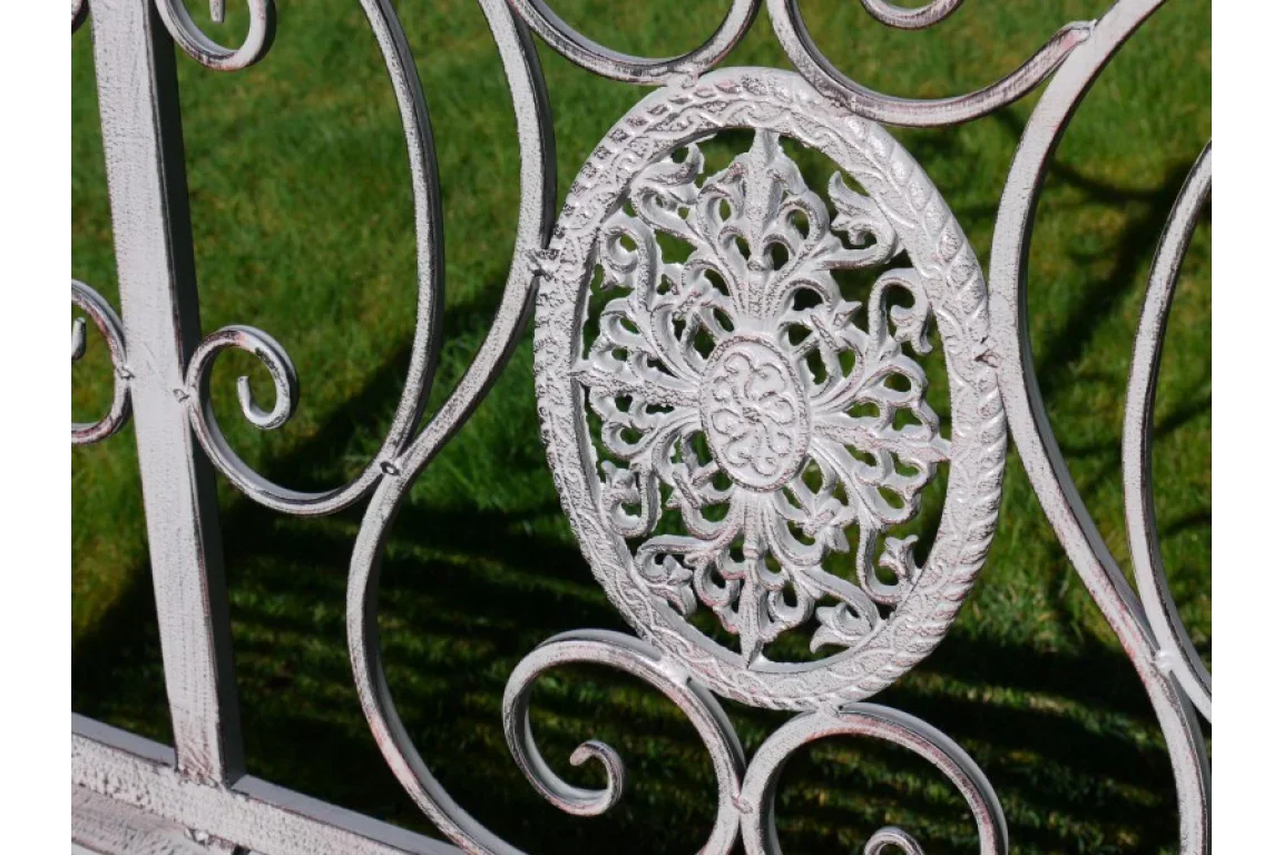 White metal garden bench with ornate floral backrest detail on grass
