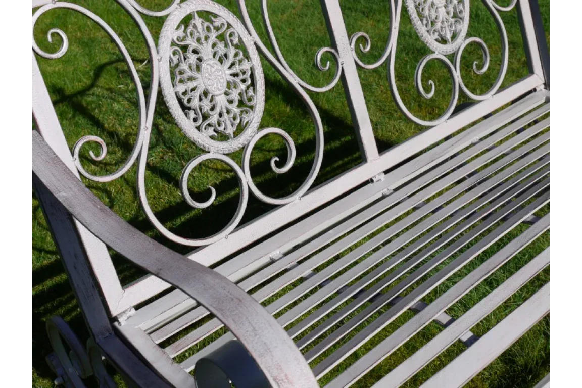 White metal garden bench with ornate scrollwork backrest on grass