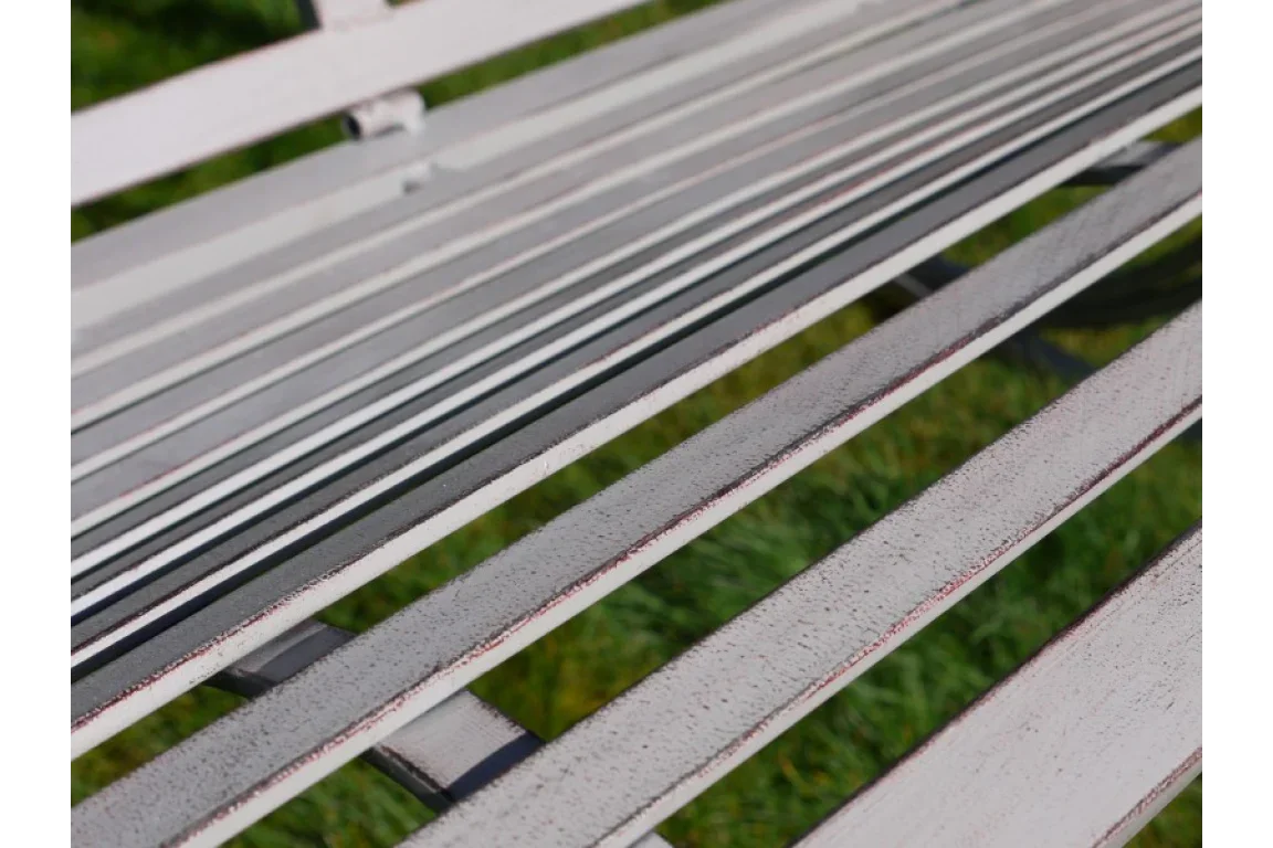 Close view of white metal bench slats with distressed finish on garden lawn