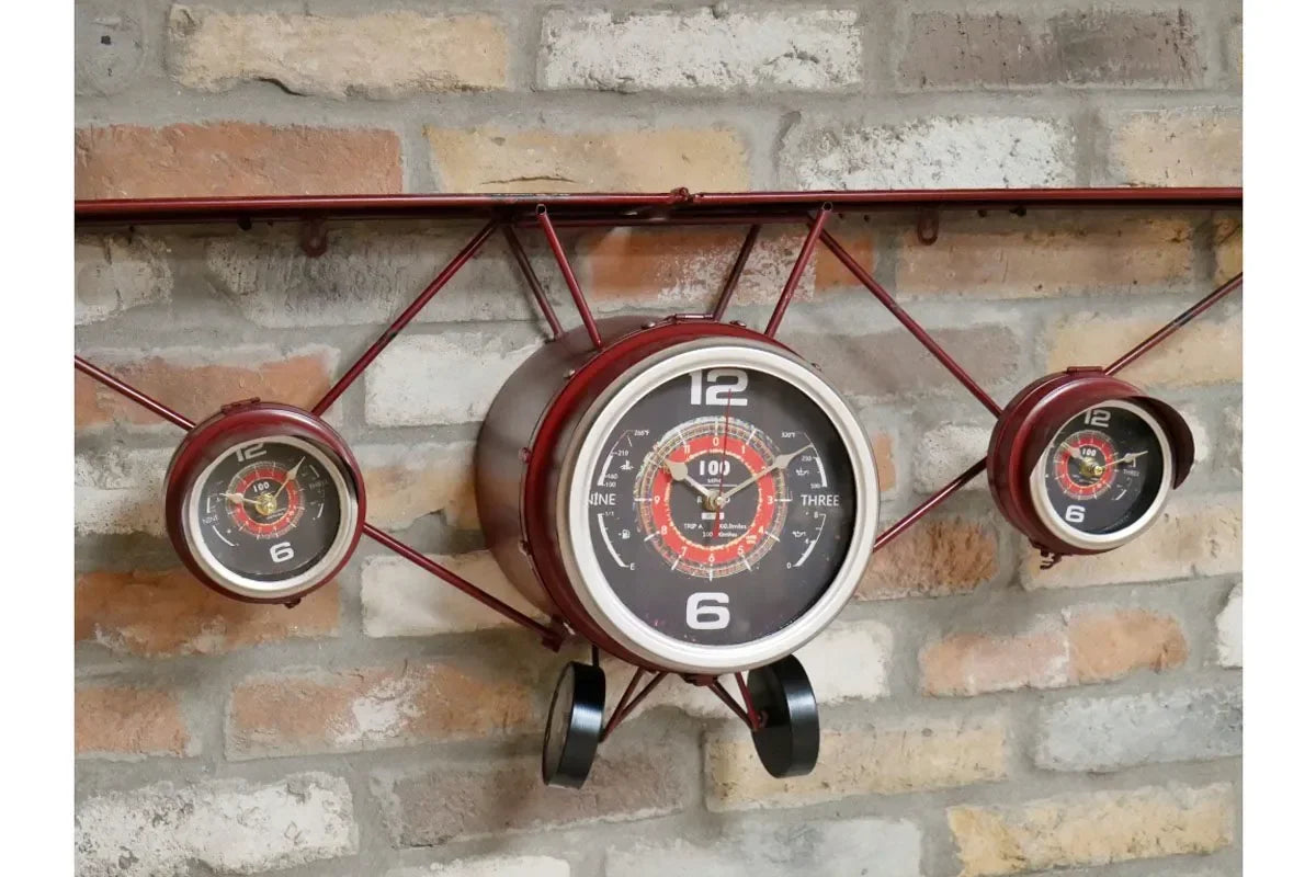 Red airplane wall clock with three dials mounted on a brick wall
