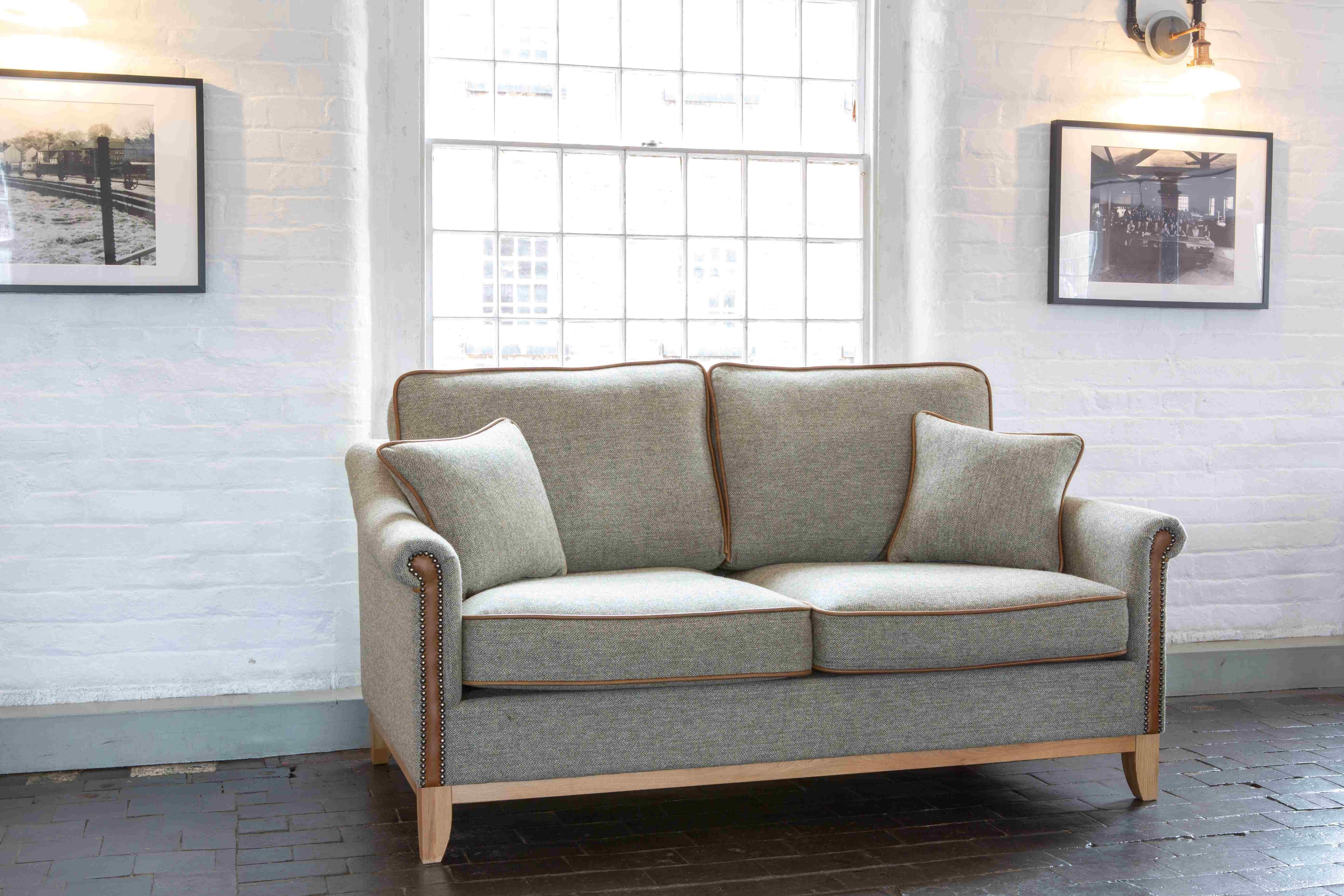 Grey fabric two-seater sofa with wooden legs and piping in a bright living room setting