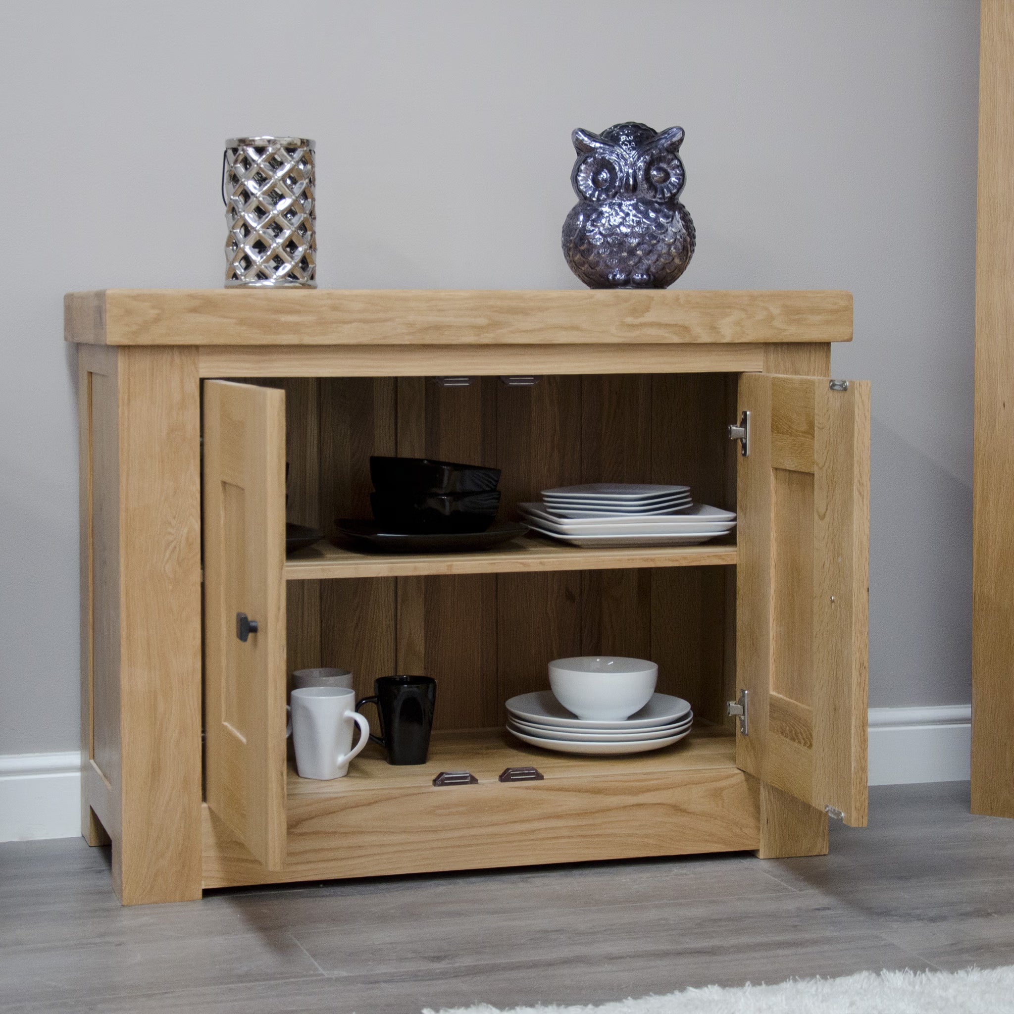 Oak sideboard with open doors showing shelves of plates, bowls, and mugs in living room