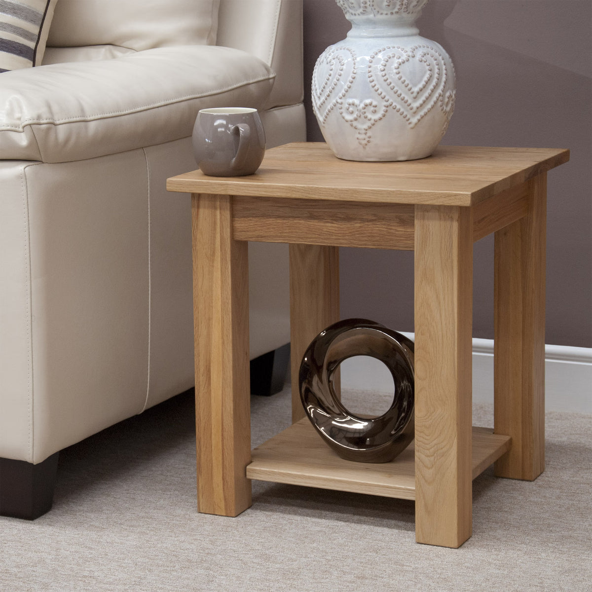 Oak side table with lower shelf beside cream sofa, ceramic mug and vase on top