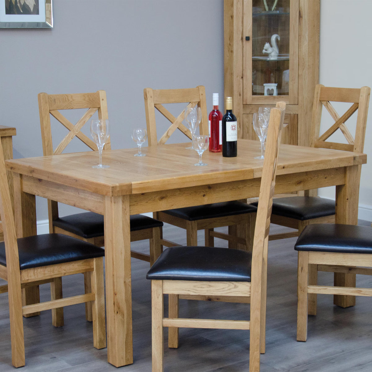 Oak dining table set with six chairs, black seat pads, wine and glasses on tabletop