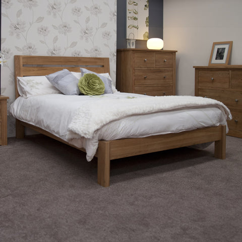 Oak bed frame with white bedding in carpeted bedroom, matching oak drawers and bedside table