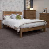 Oak bed frame with white bedding in carpeted bedroom, matching oak drawers and bedside table