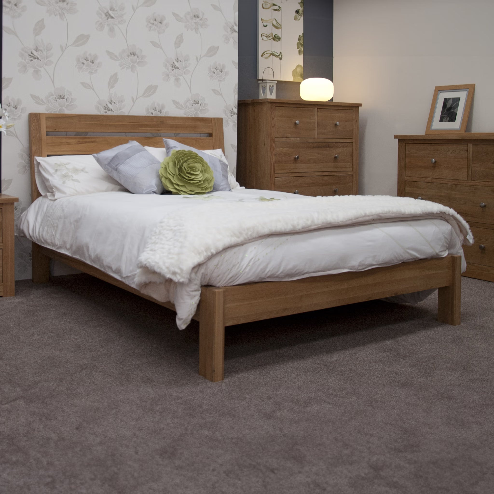 Oak bed frame with white bedding in carpeted bedroom, matching oak drawers and bedside table