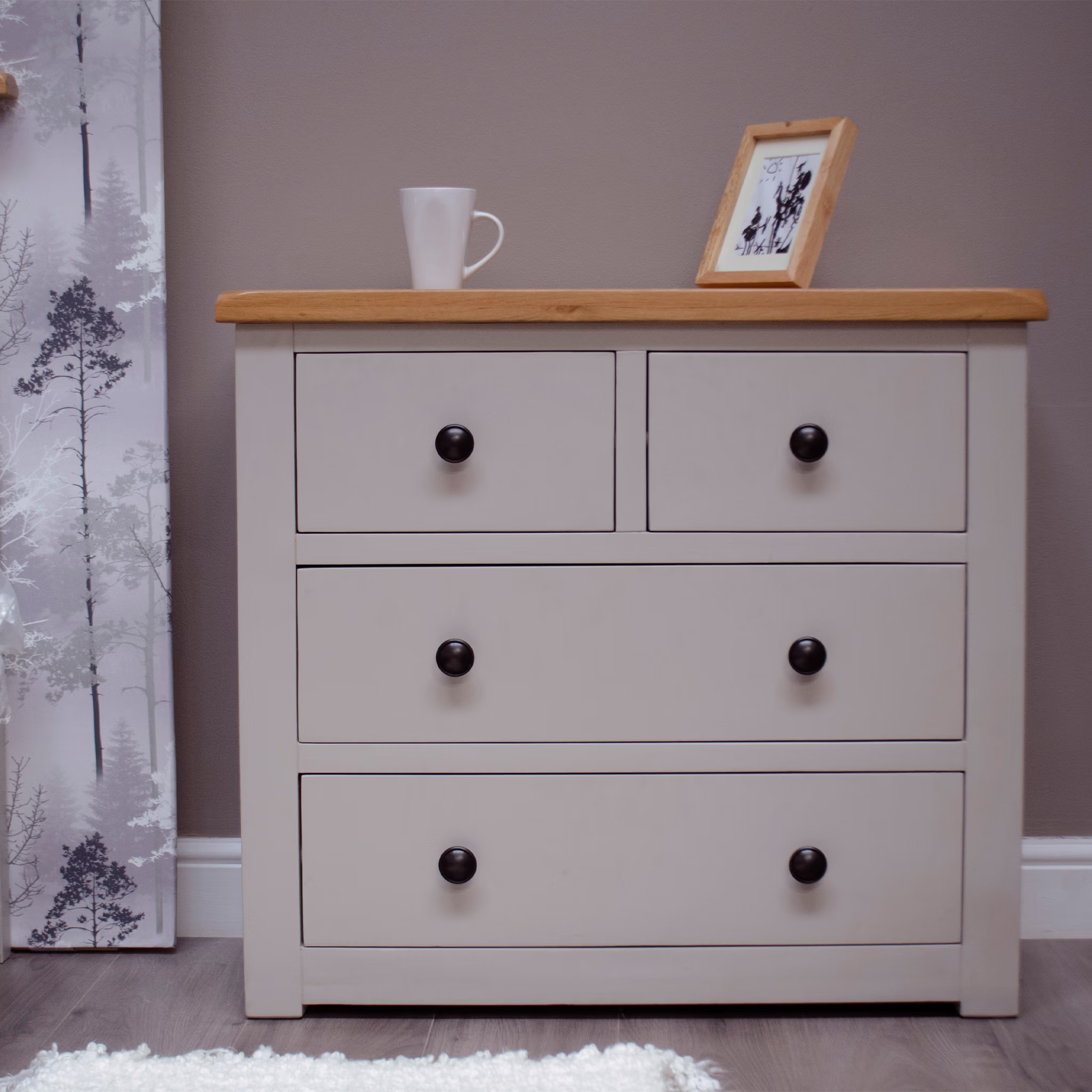 Beige chest of drawers with wooden top, black knobs, cup and photo frame on dresser