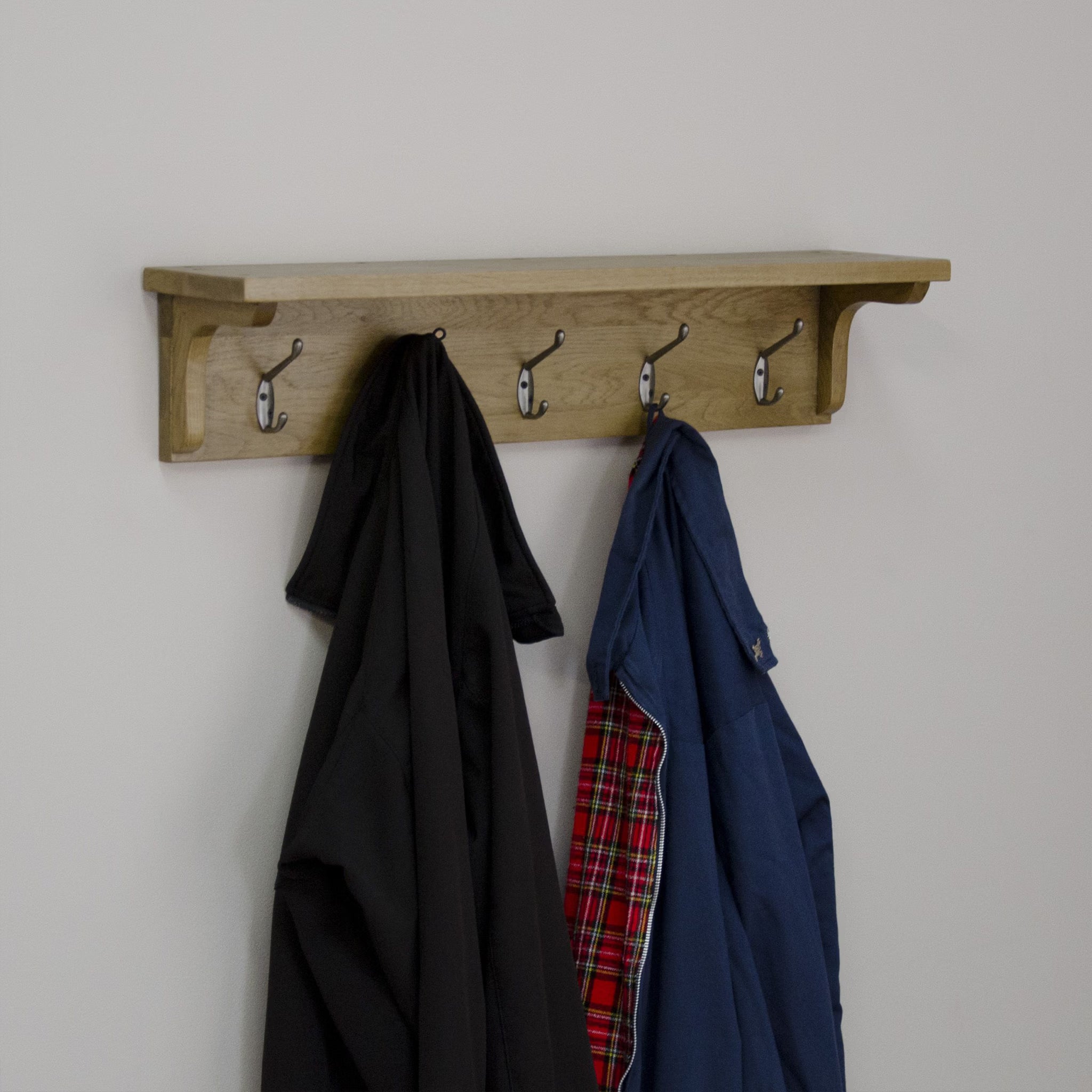 Oak wall mounted coat rack with four metal hooks holding jackets