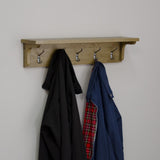 Oak wall mounted coat rack with four metal hooks holding jackets
