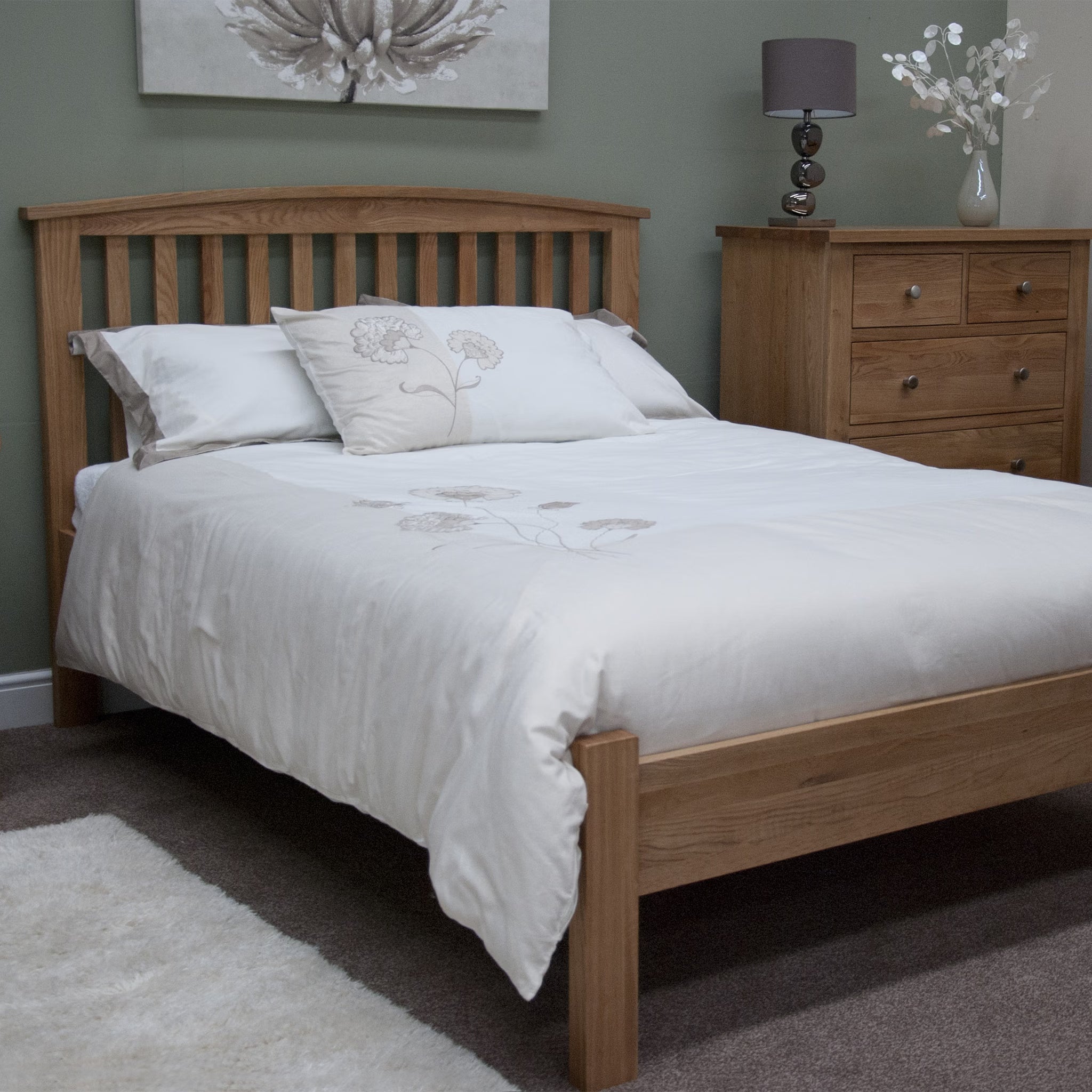 Oak wooden bed frame with white floral bedding in a cosy bedroom setting