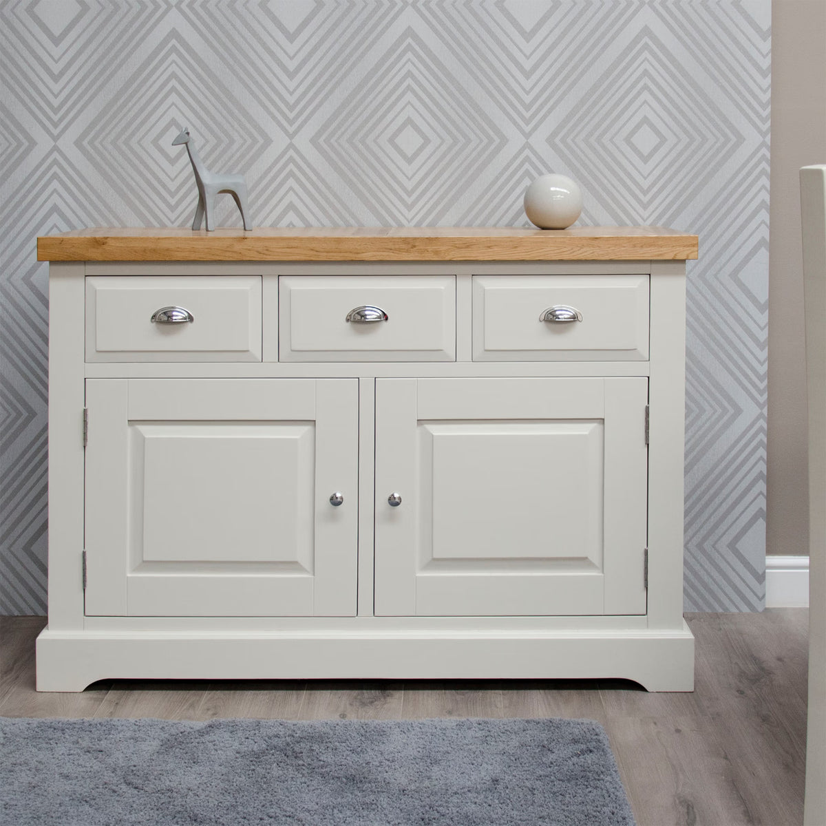 Cream sideboard with oak top, three drawers, chrome handles, and geometric wallpaper backdrop
