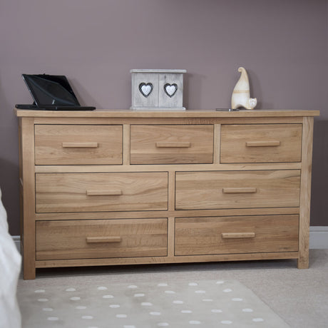 Oak chest of drawers with seven handles placed against a mauve wall on carpeted floor