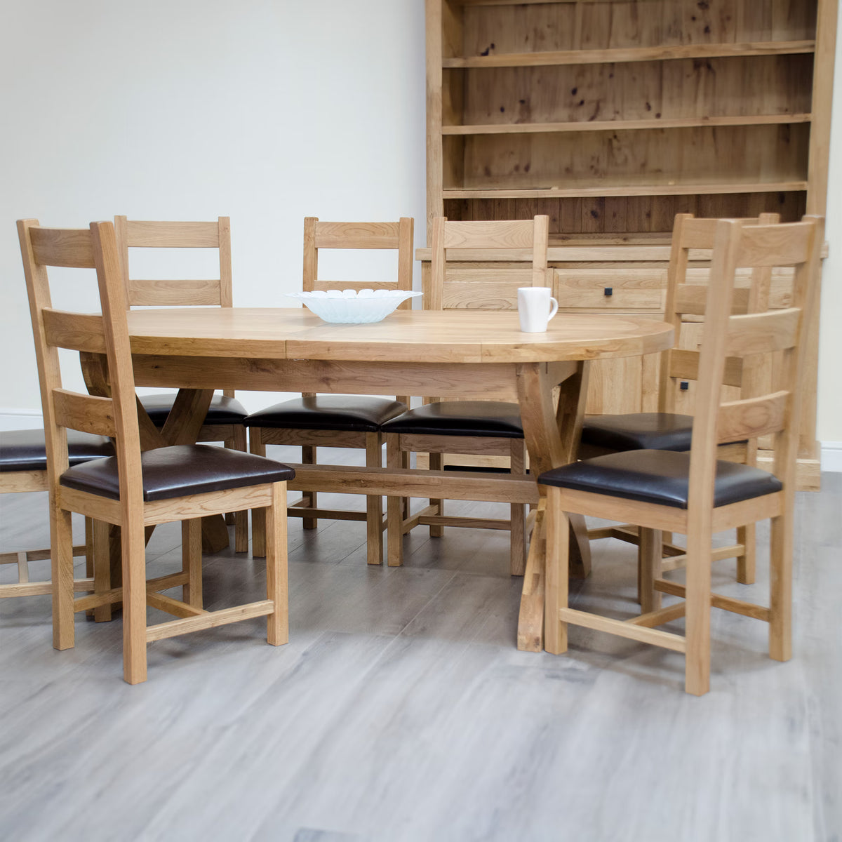 Solid oak dining table set with six matching chairs and dark seat pads on wood flooring
