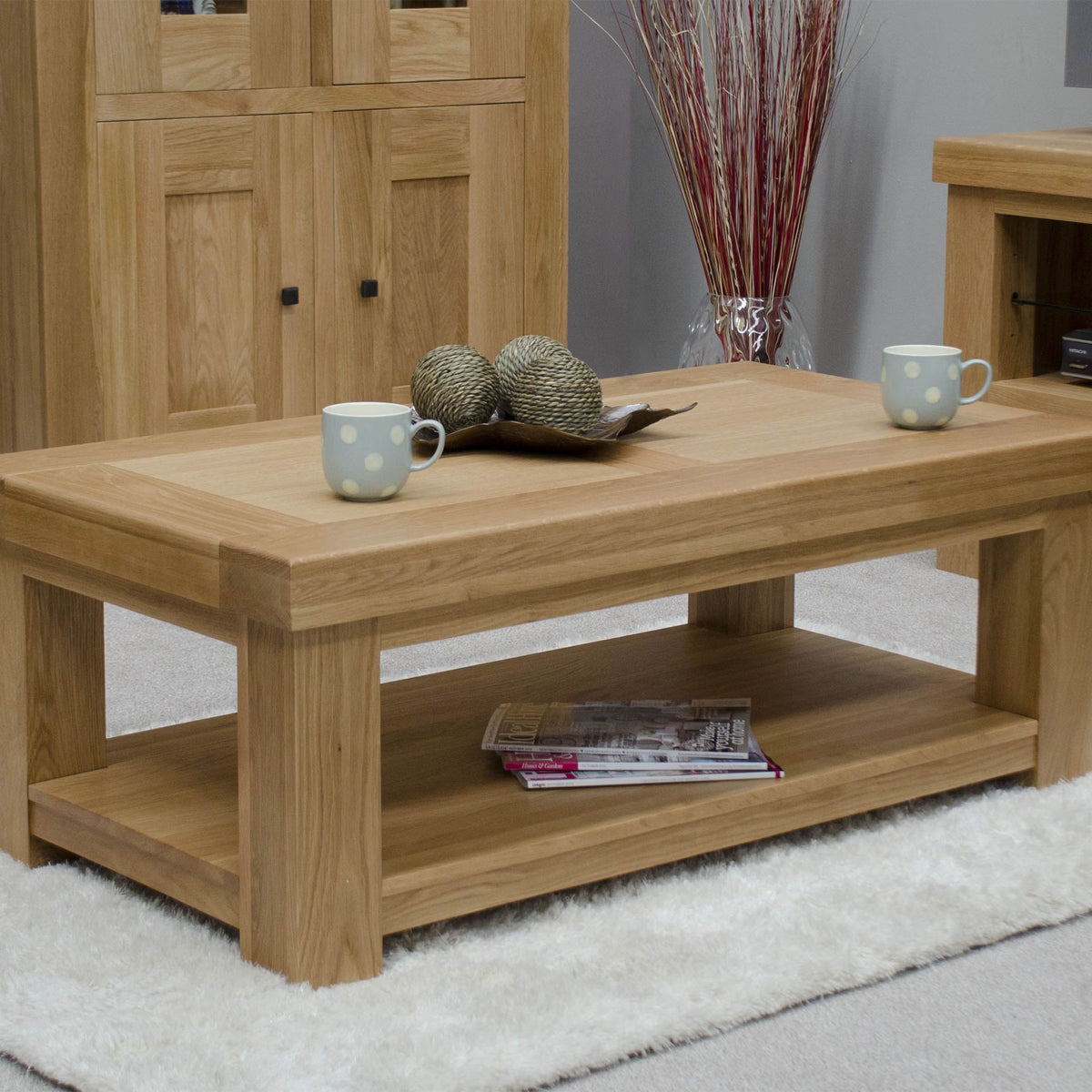 Oak coffee table with shelf, two mugs, magazines on lower shelf, living room setting