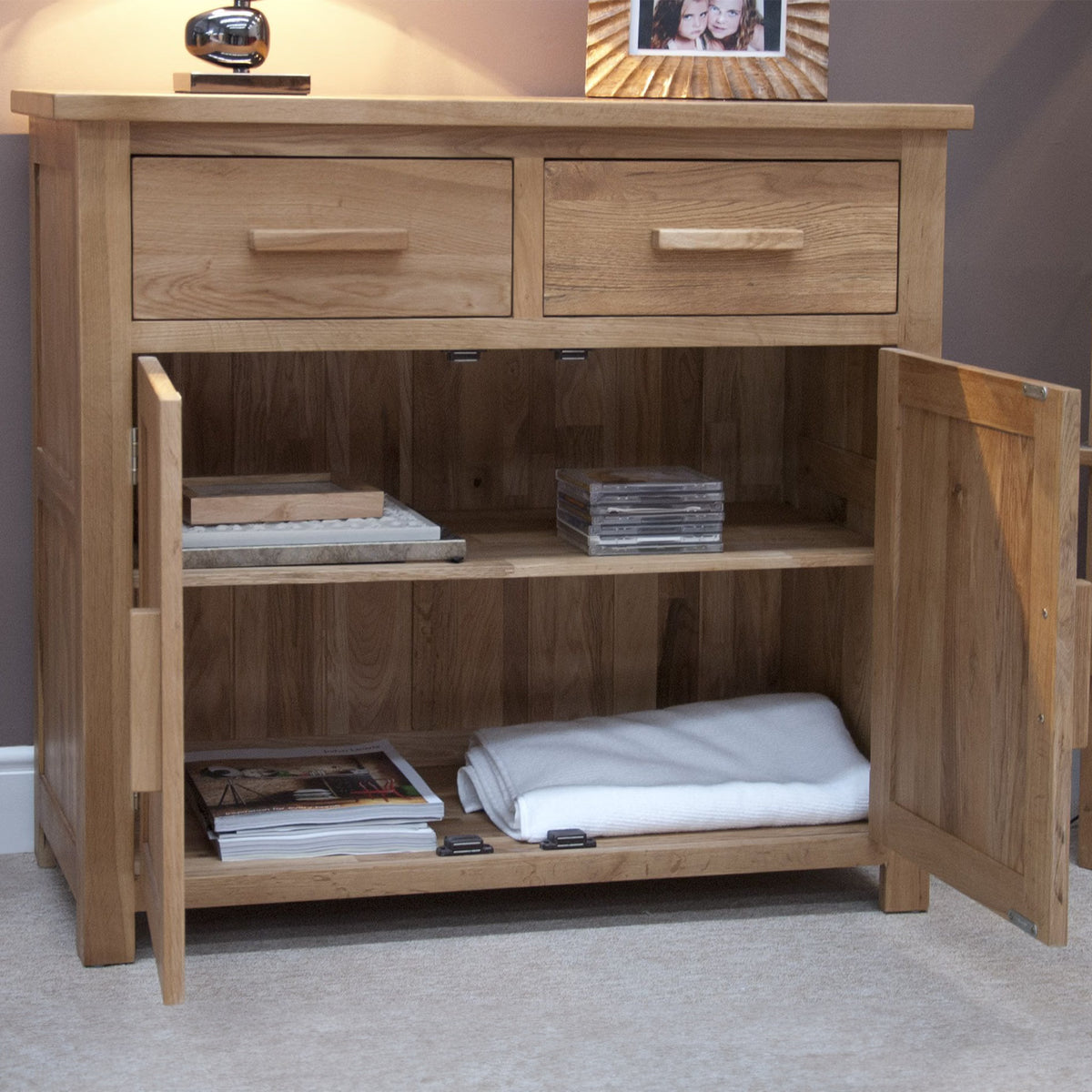 Oak sideboard cabinet with two drawers and open double doors, shelves holding books and linen
