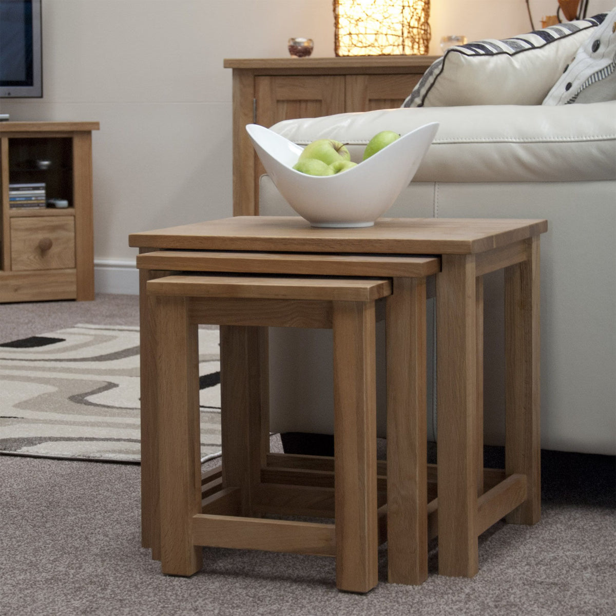 Oak nesting tables set beside sofa with white fruit bowl in living room