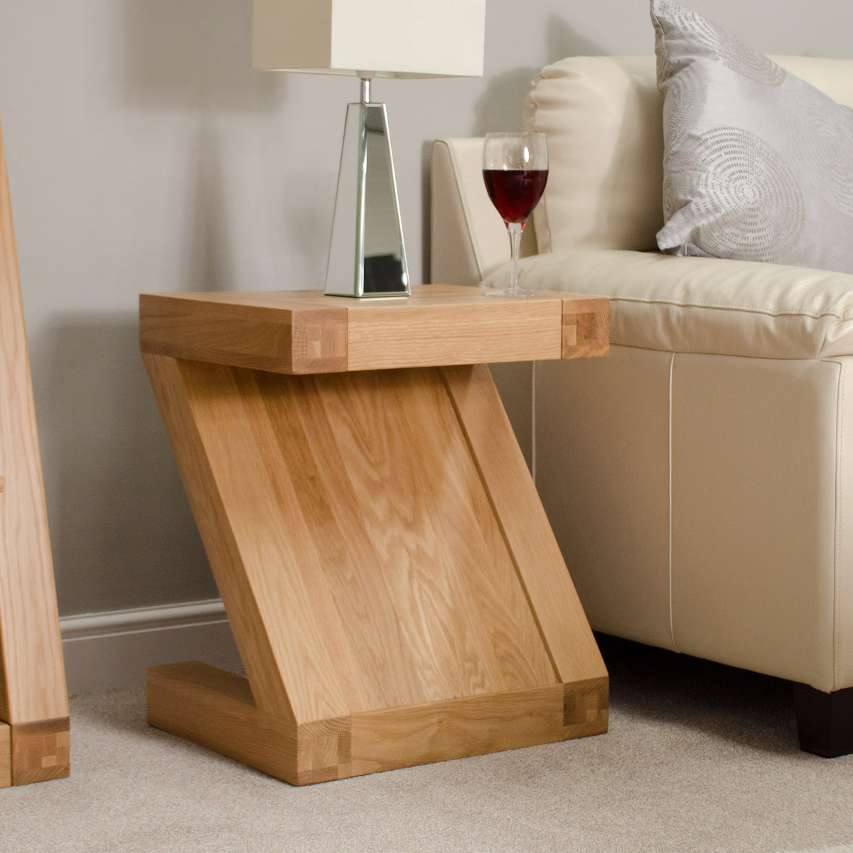 Oak side table with modern Z-shaped design beside cream sofa, topped with lamp and wine glass