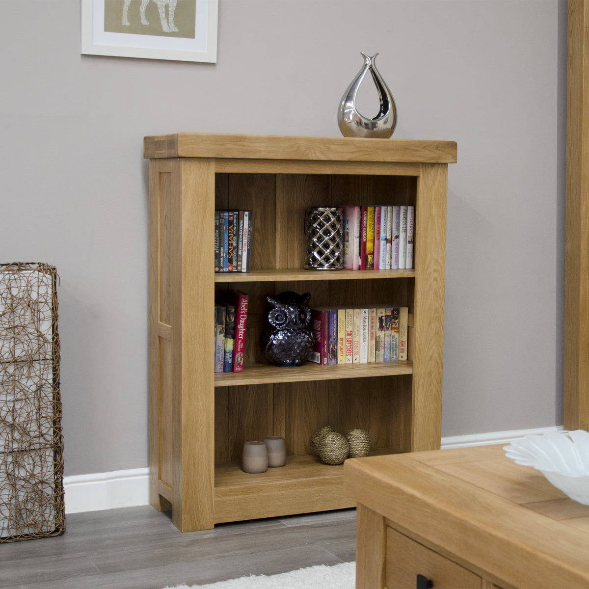 Light oak bookcase with three shelves, books, ornaments, and decorative vase