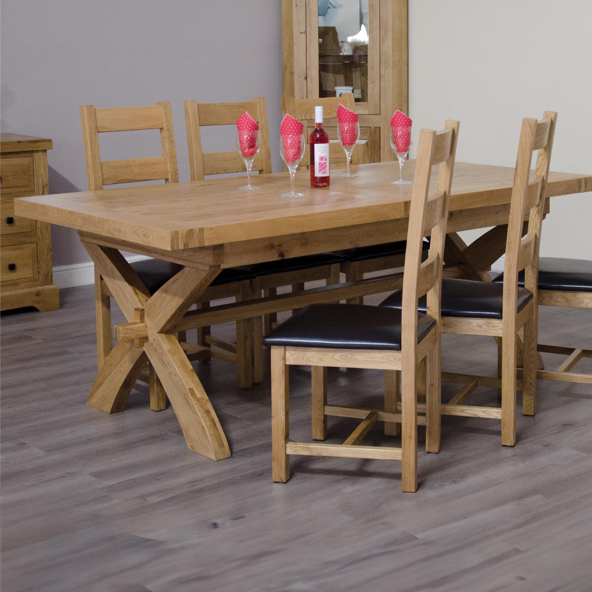 Oak dining table with cross legs and four matching chairs on grey wood floor