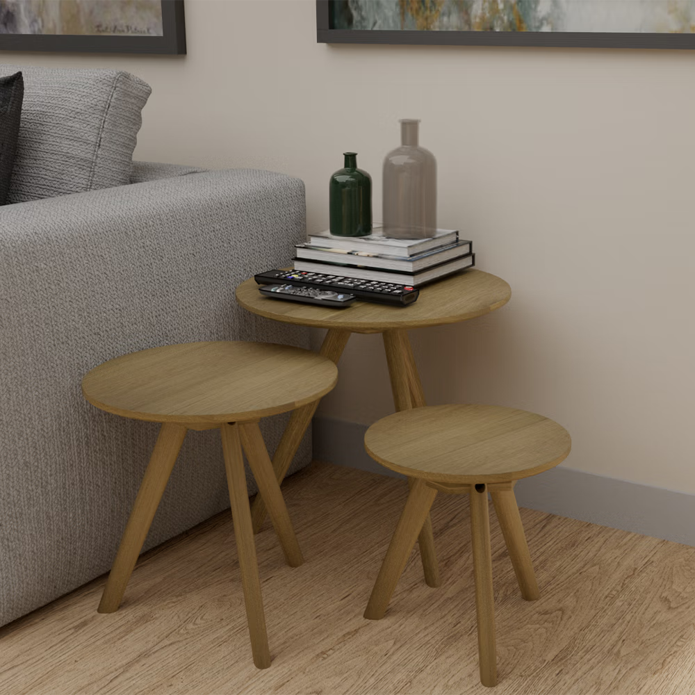 Set of three round oak nesting tables beside grey sofa with books and vases on top