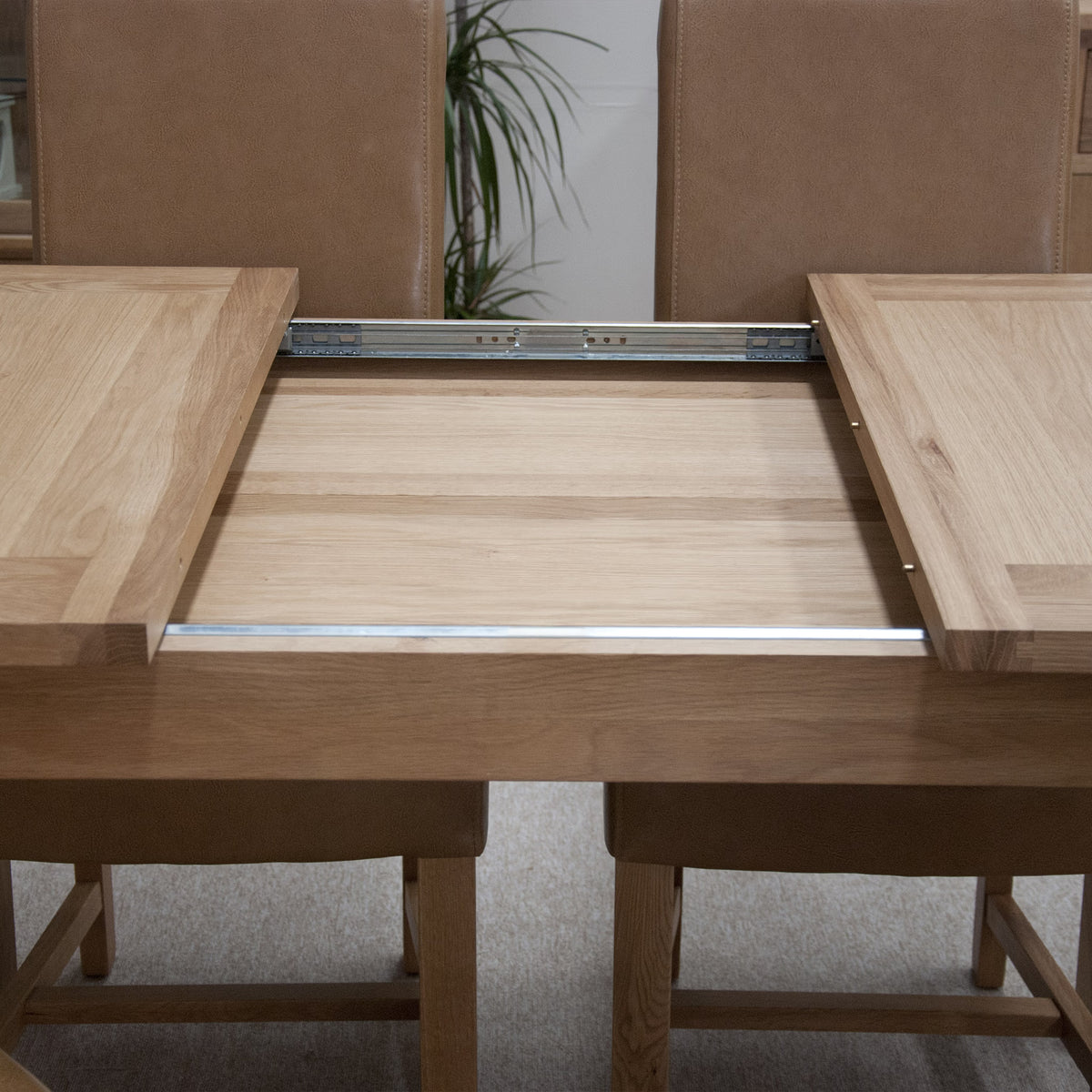 Oak extending dining table with slide-out leaf mechanism and brown upholstered chairs