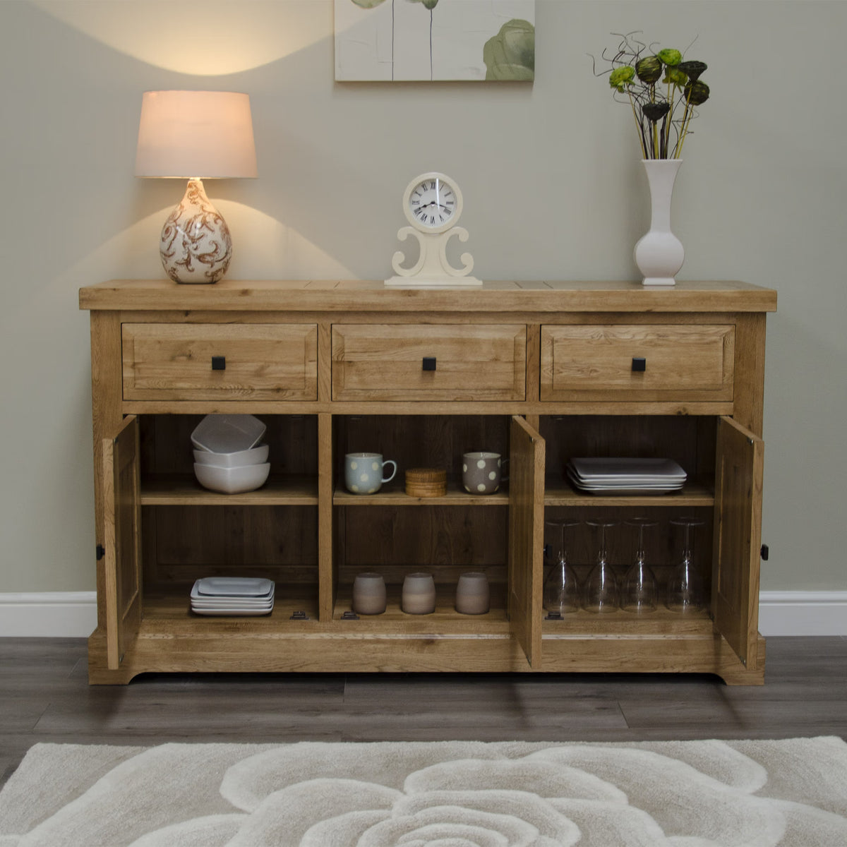 Oak sideboard with three drawers and open cupboard doors displaying dishes and glassware