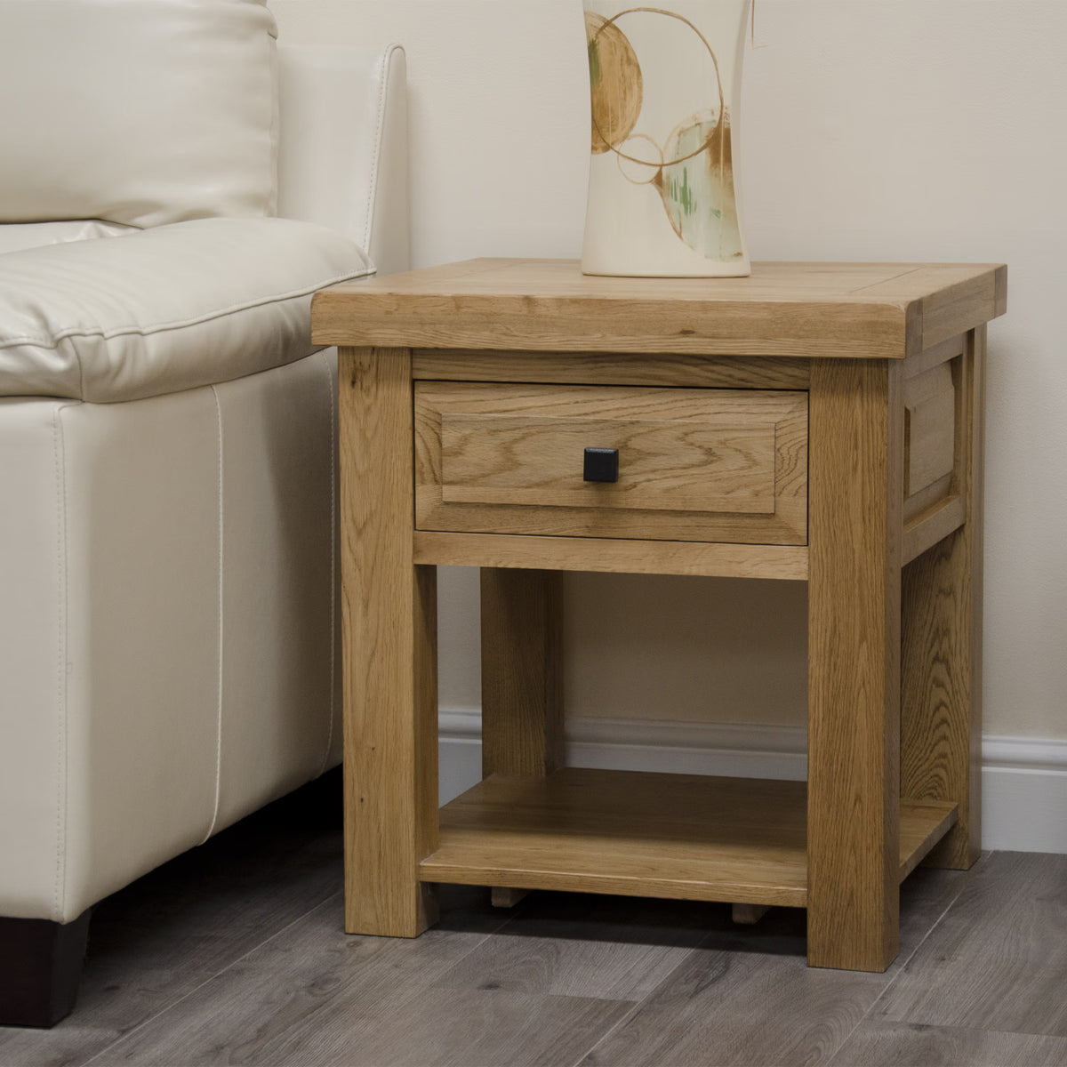 Oak bedside table with single drawer and lower shelf beside cream sofa on wood floor