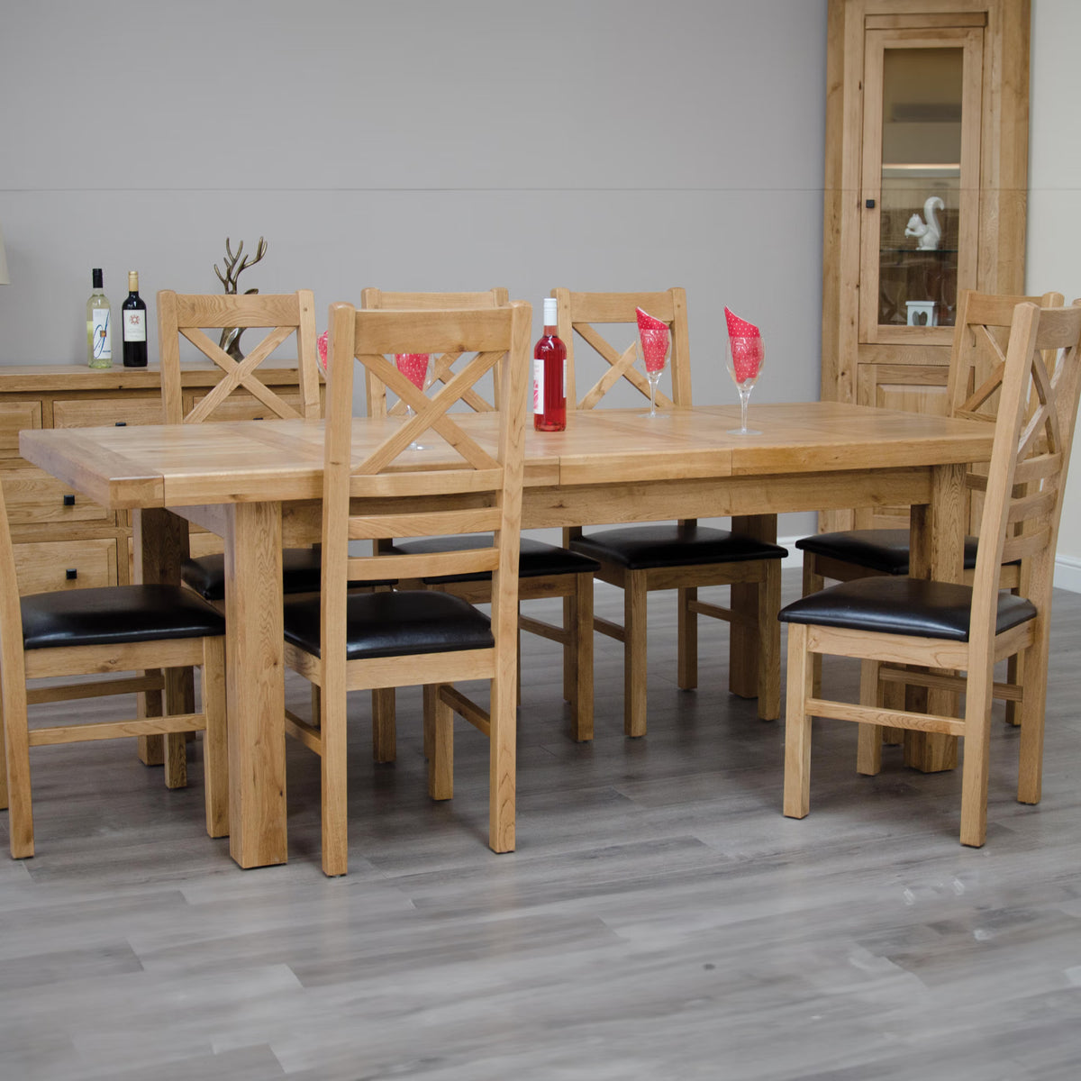 Oak dining table set with six wooden chairs and black seat cushions on wood floor