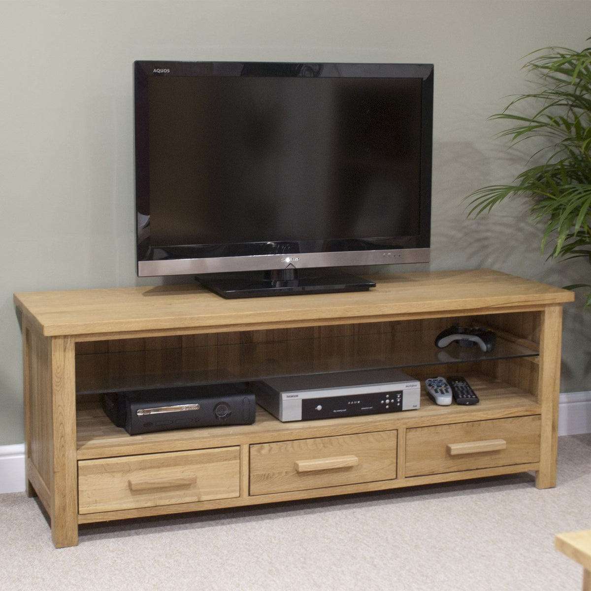 Oak TV unit with three drawers and open shelf, holding console, remotes, and media equipment