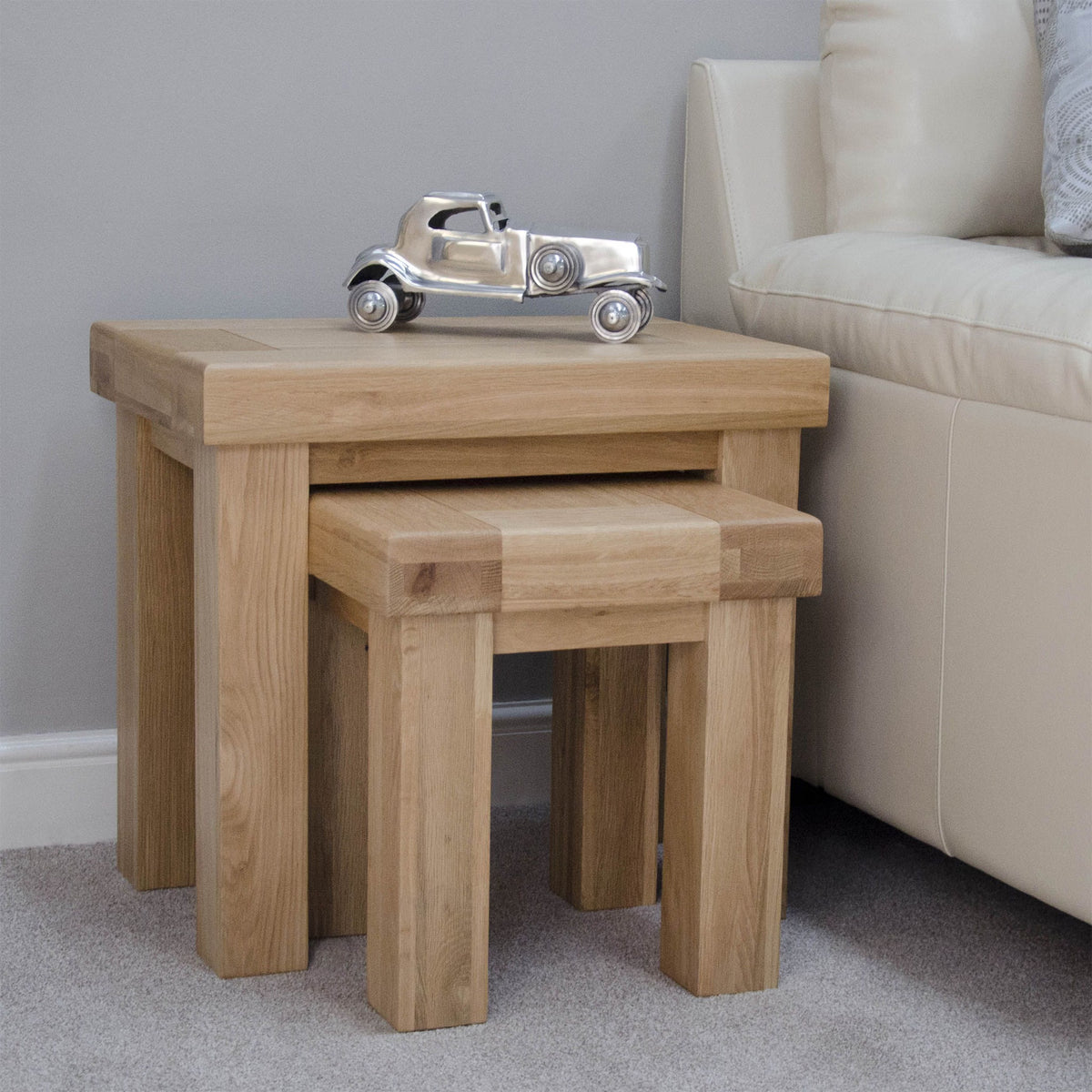 Oak nesting tables beside cream sofa with metal decorative car on top