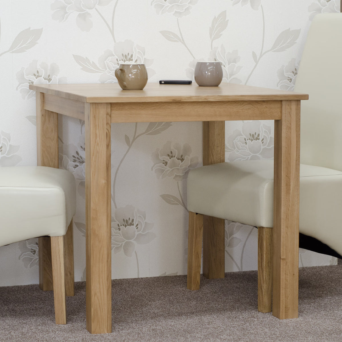 Oak dining table with two cream chairs and mugs on top, set on carpeted floor
