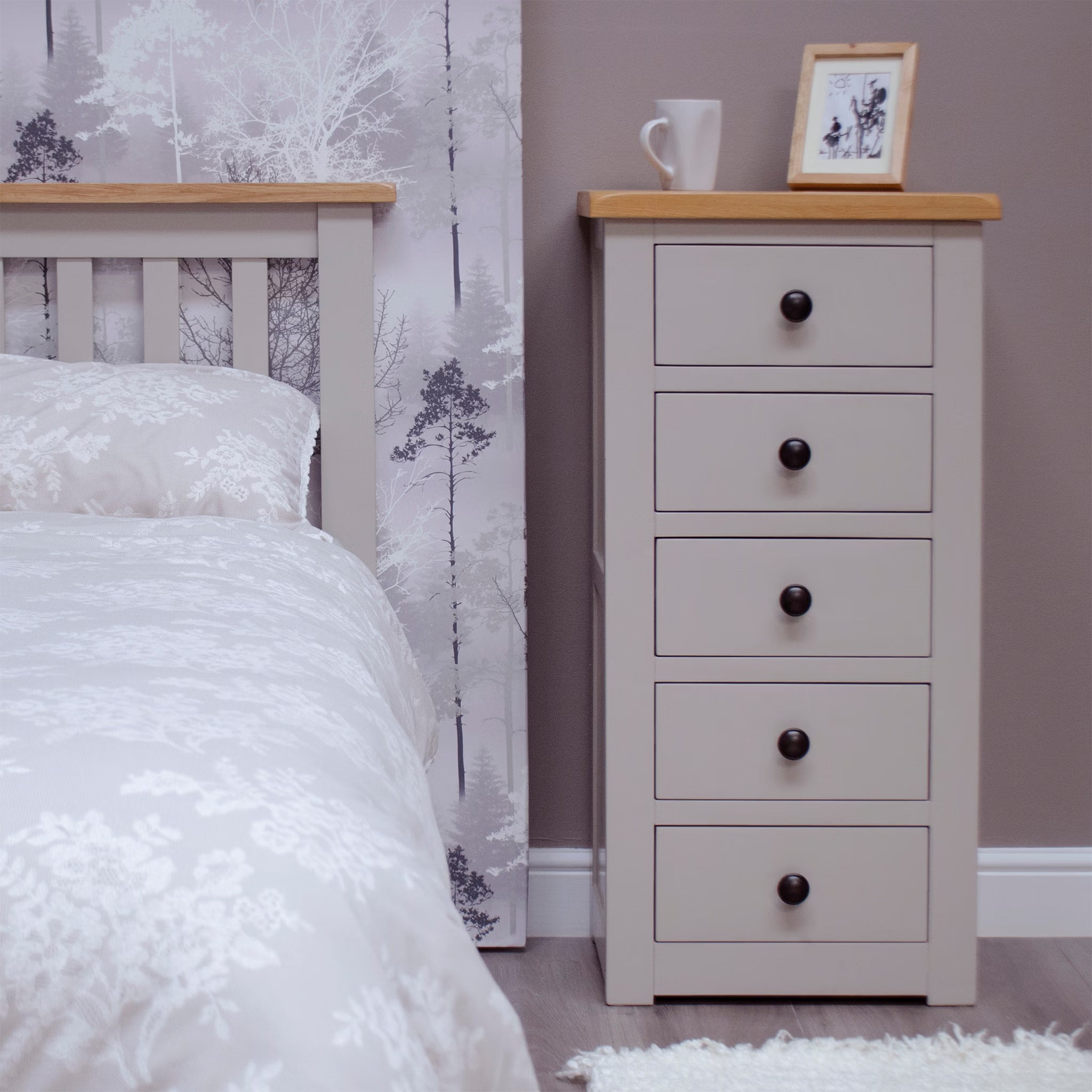 Light grey wooden chest of drawers with oak top beside a matching bed and white bedding