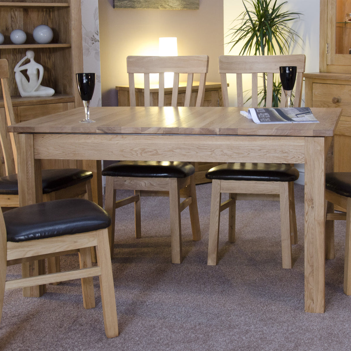 Oak dining table set with four chairs and black cushioned seats in a carpeted room