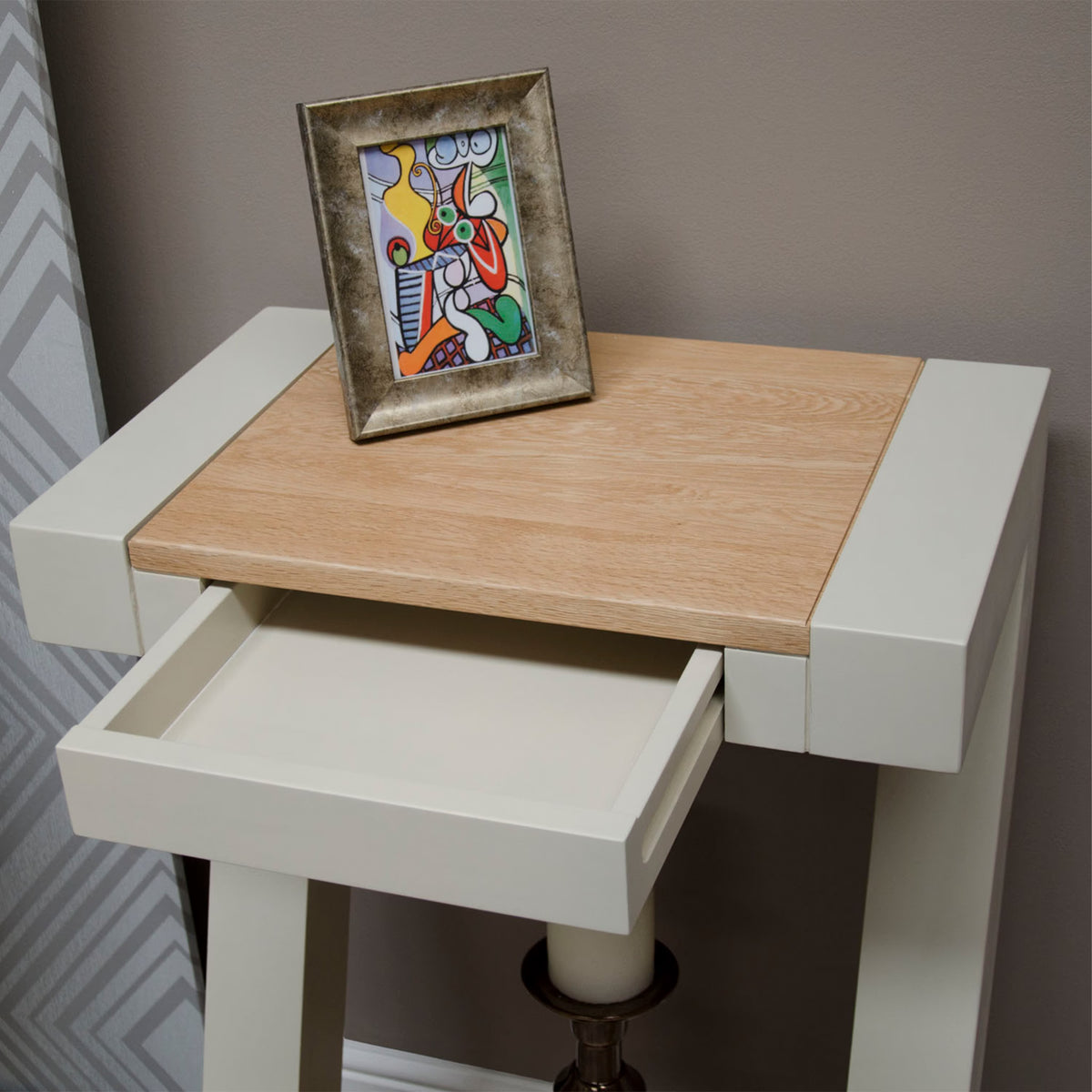 Cream console table with light wood top, single open drawer, framed art resting on surface