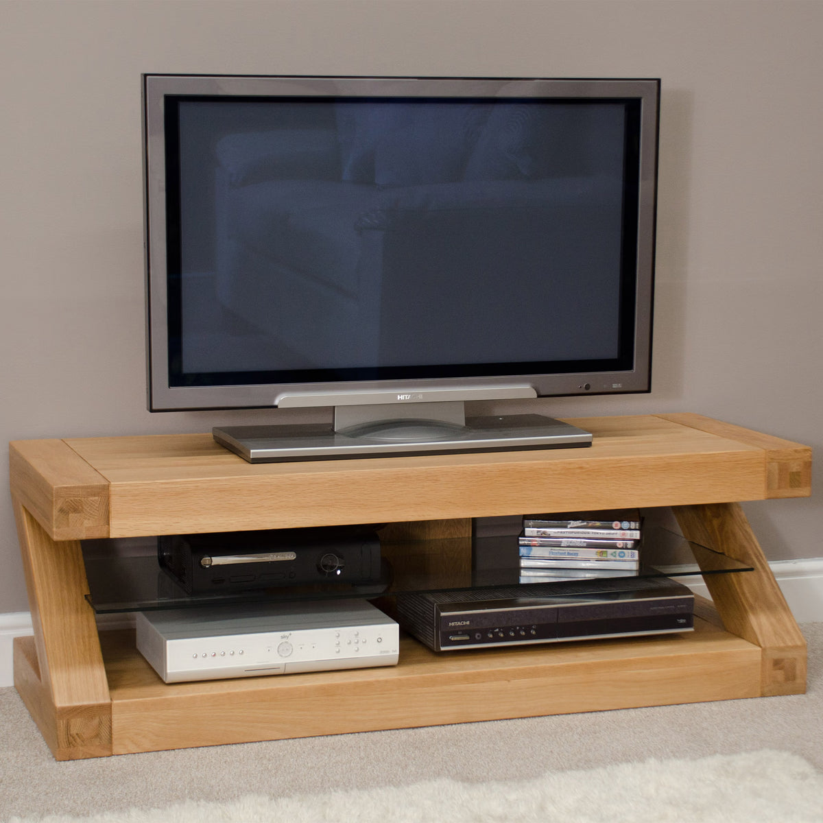 Oak TV unit with glass shelf, holding entertainment devices and DVDs, set against grey wall