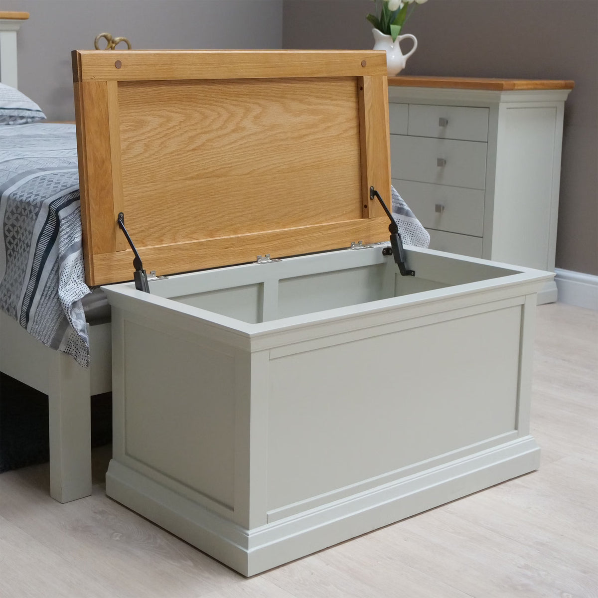 Wooden blanket box with oak lid open at end of bed in bedroom