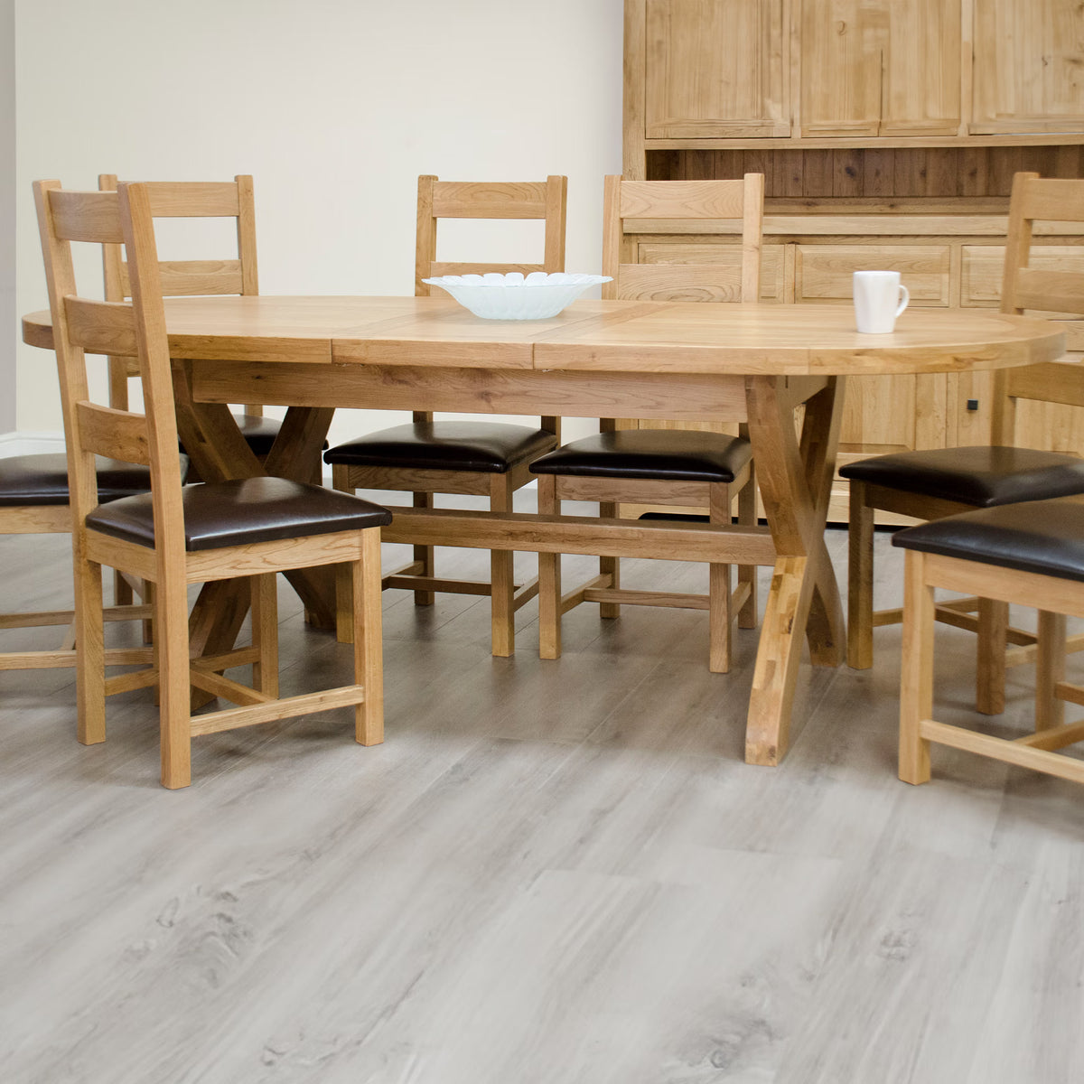 Oak dining table set with six wooden chairs and dark cushions on light wood floor