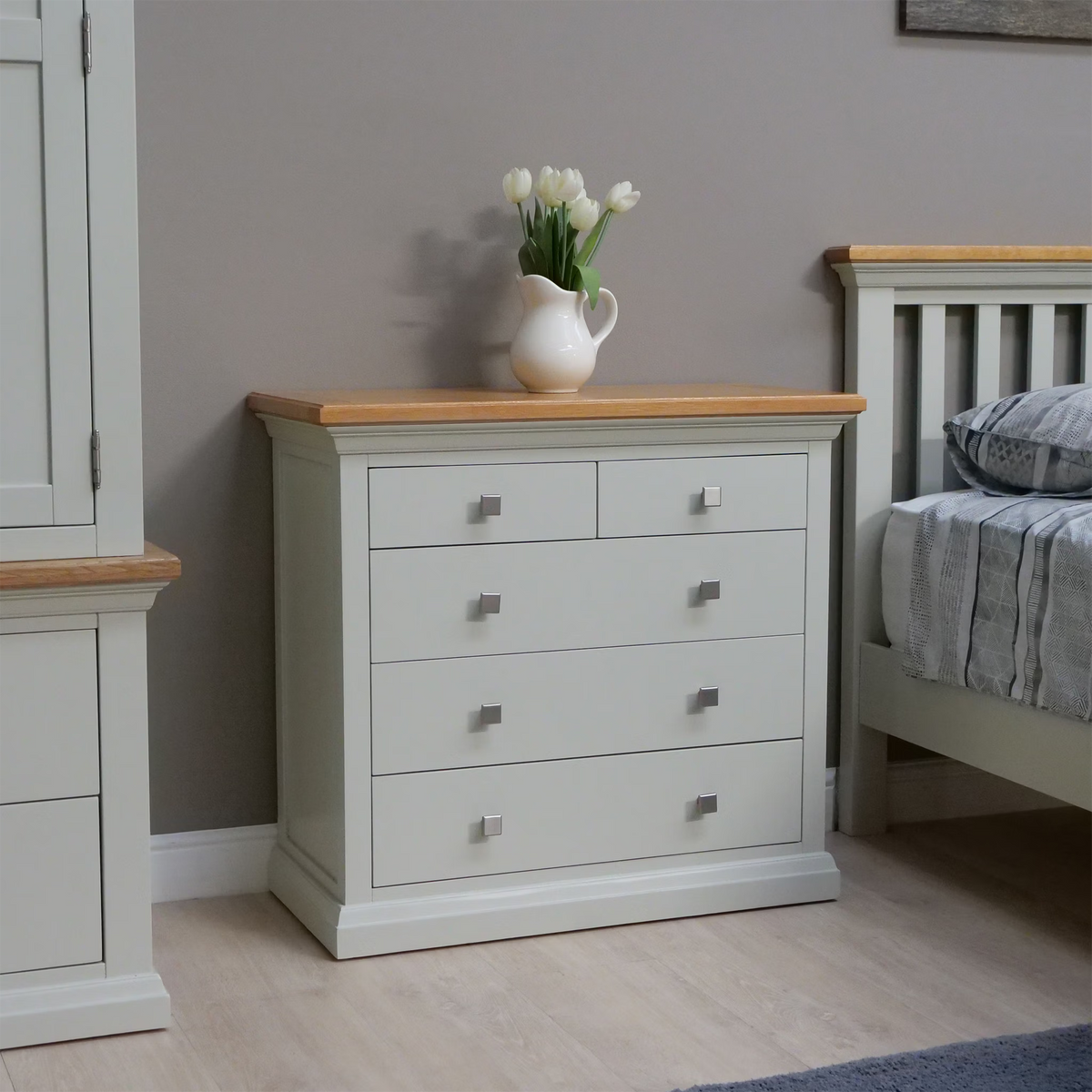 Light grey chest of drawers with oak top and silver handles beside a bed in bedroom