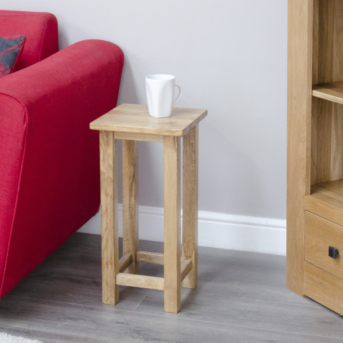 Oak side table with straight legs beside red sofa and white mug on top