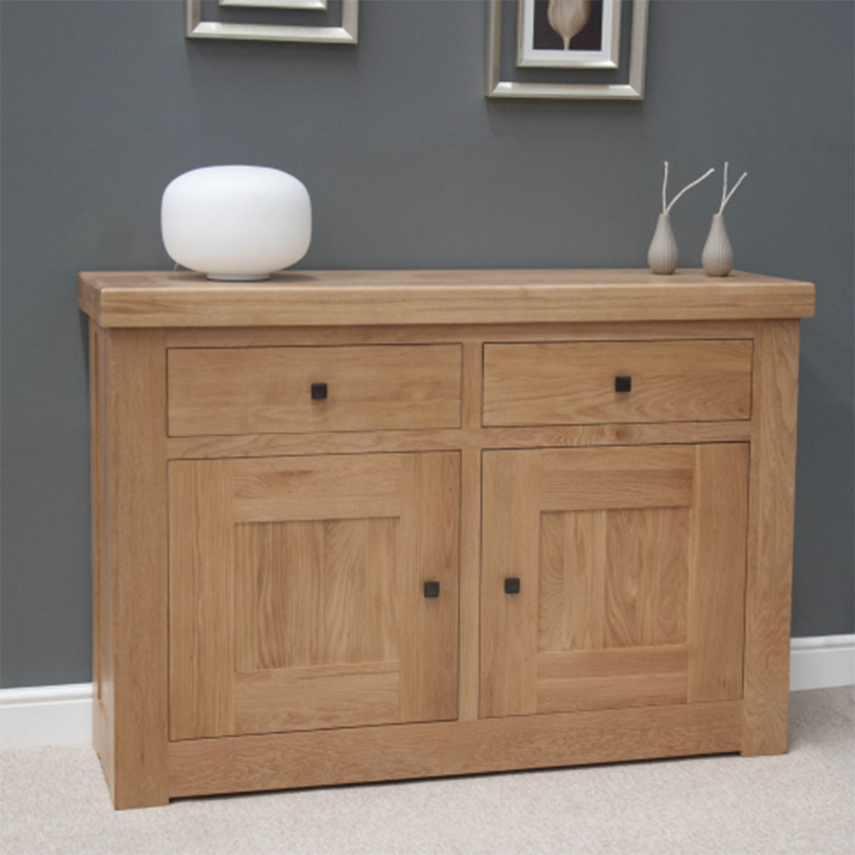 Oak sideboard with two drawers and two doors against grey wall, modern decor accents on top