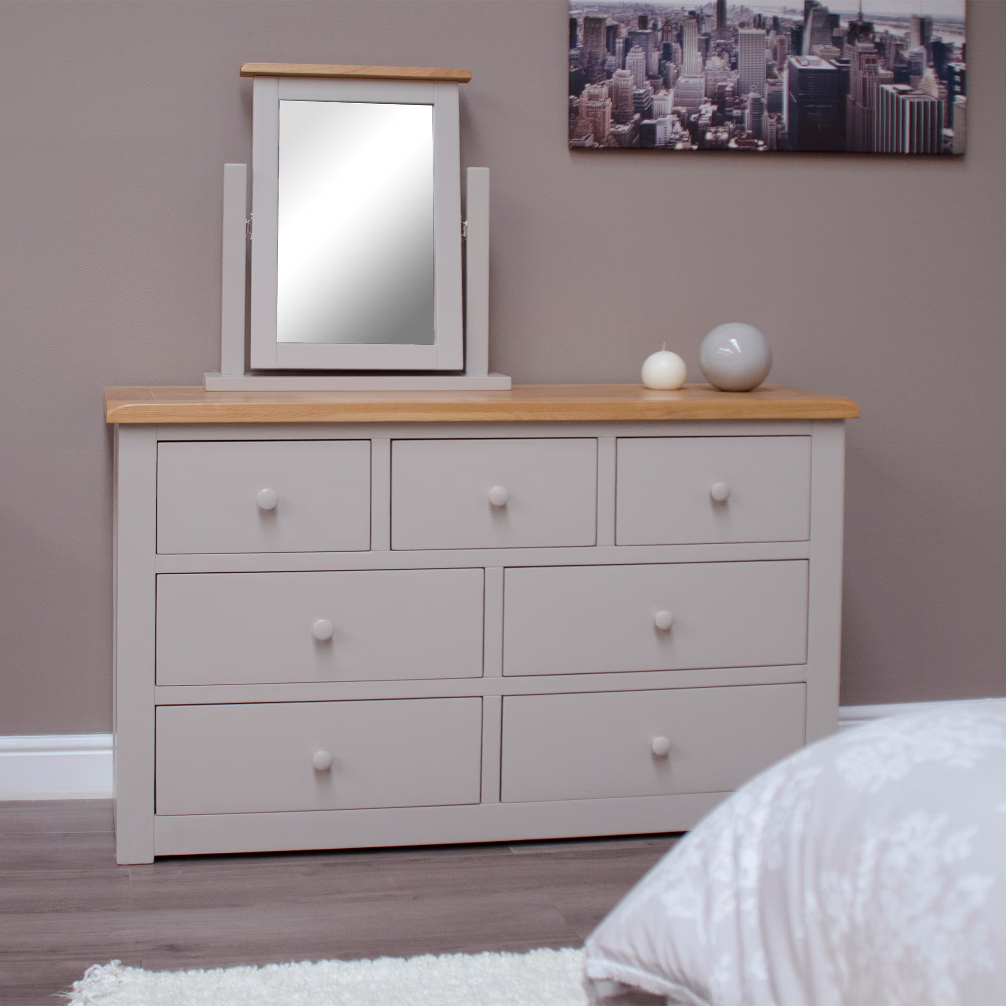 Grey wooden chest of drawers with oak top, tabletop mirror, and decorative bedside ornaments