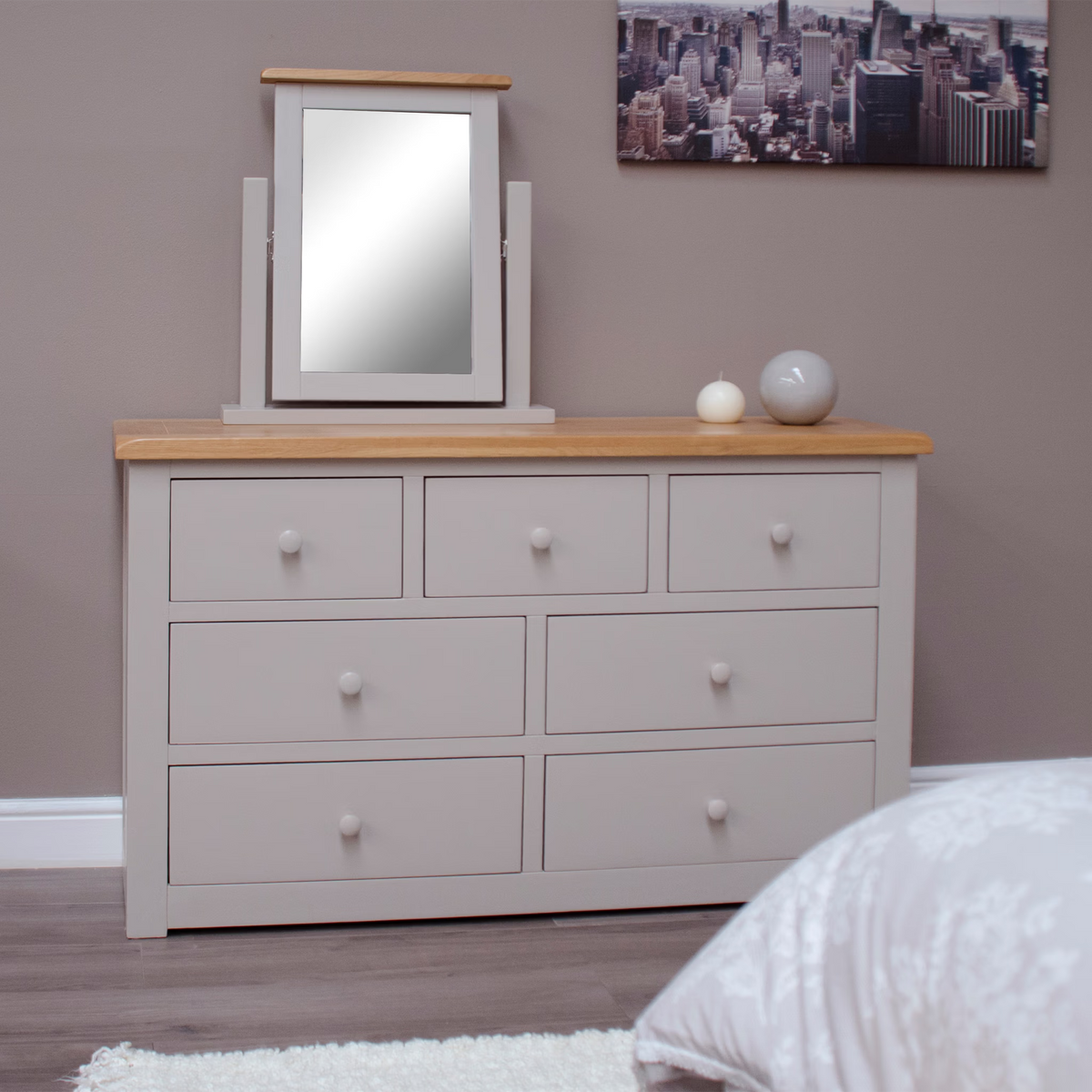 Grey wooden chest of drawers with oak top, tabletop mirror, and decorative bedside ornaments