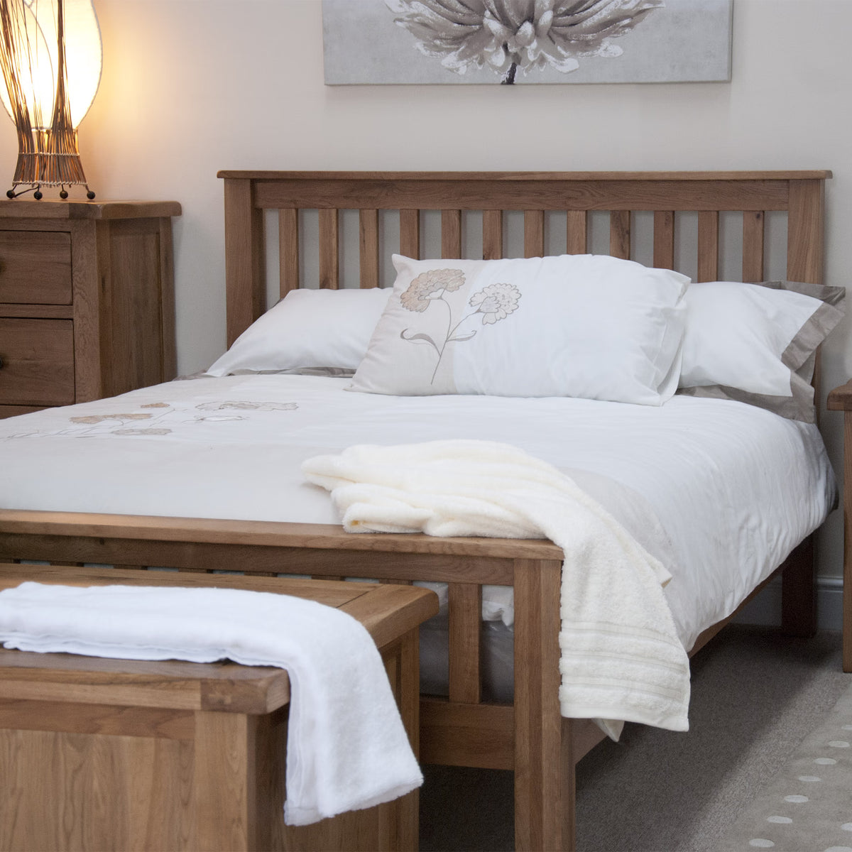 Wooden bed frame with white bedding and matching bedside cabinet in cosy bedroom setting