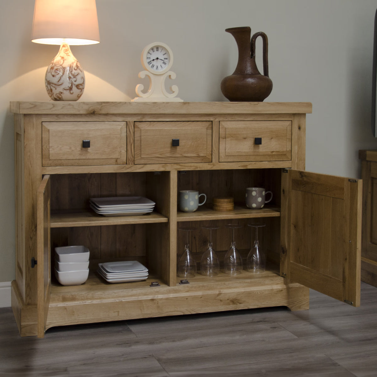 Oak sideboard with three drawers, open doors showing shelves with plates and glassware