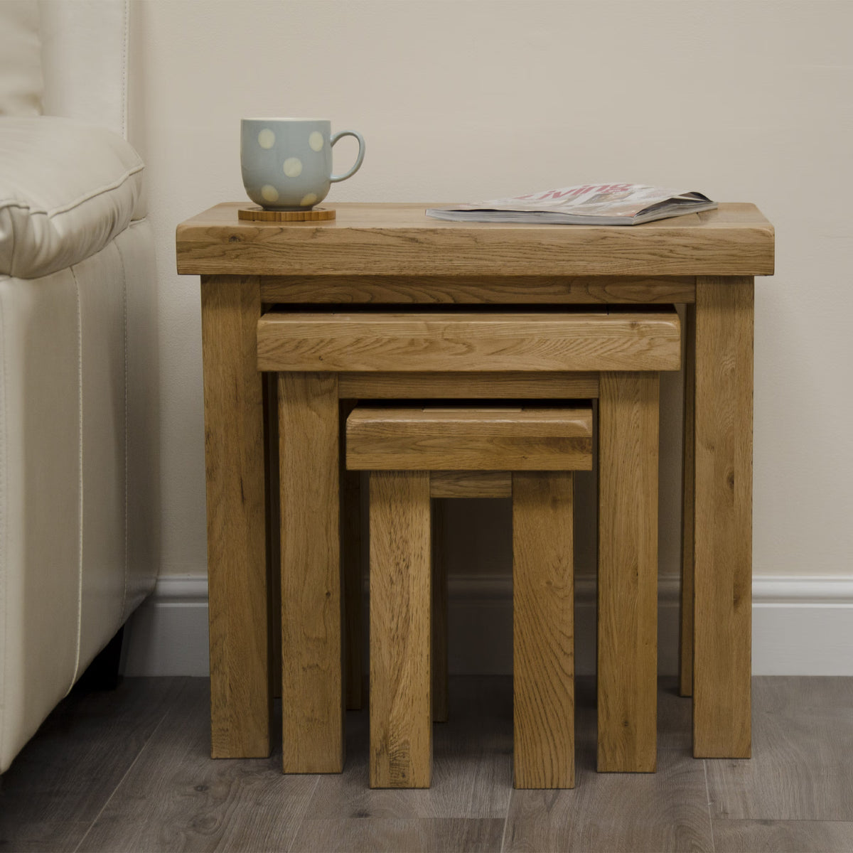 nest of oak tables with magazine and mug beside sofa on wooden floor